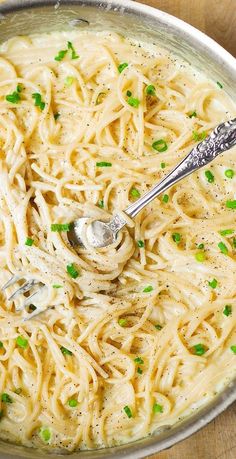 a bowl filled with pasta and peas on top of a wooden table next to a spoon