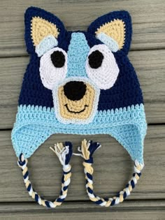 a crocheted bear hat with ear flaps on top of a wooden surface,