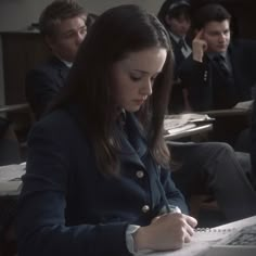 a group of people sitting at desks in a classroom with one writing on a piece of paper