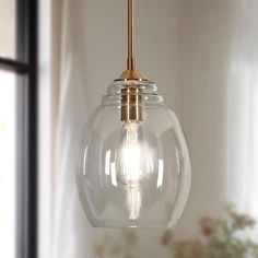 a clear glass light hanging from a gold colored ceiling fixture over a window sill