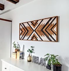 a wall hanging above a white dresser with plants and other items on top of it