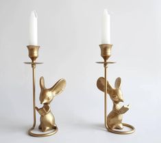 two gold candlesticks that have animals on them and one has a candle in the shape of a mouse