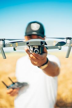 a man holding a remote control in his hand while flying a small aircraft over a field