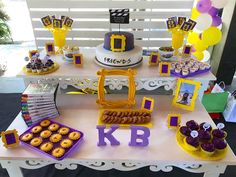 a table topped with cakes and desserts on top of a white table covered in purple and yellow decorations