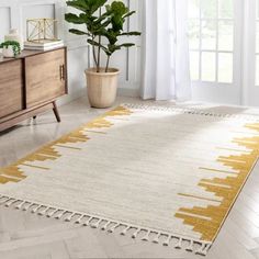 a white and yellow rug with tassels on the floor next to a potted plant