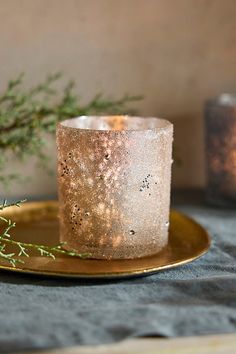 a lit candle sitting on top of a gold plate next to a small tree branch