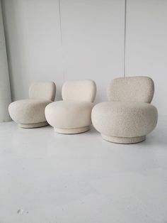 three white chairs sitting next to each other on top of a cement floor in front of a window