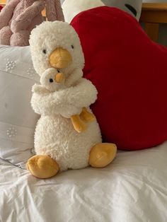 a stuffed animal sitting on top of a bed next to two pillows and a red heart