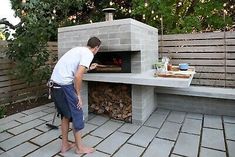 a man standing in front of a brick oven on top of a stone patio next to a tree