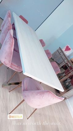 a table and chairs with pink velvet upholstered on the backrests, in front of a mirrored wall