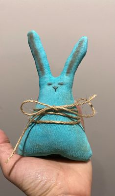 a hand holding a small blue stuffed animal with twine around it's ears