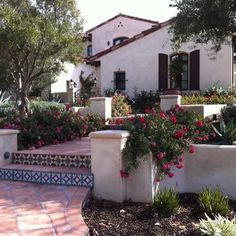 a white house with red flowers in the front yard and steps leading up to it