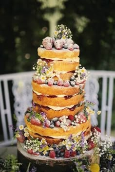 a wedding cake with flowers and berries on top is sitting on a table in front of a white chair