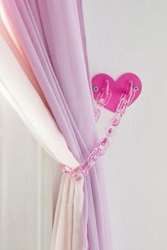 a pink heart shaped object hanging on the side of a window sill next to sheer curtains