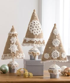 three crocheted christmas trees sitting on top of a wooden table next to ornaments