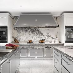 a kitchen with marble counter tops and stainless steel appliances, including an oven hood over the range