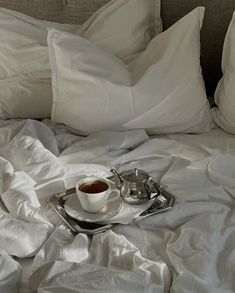 a cup of coffee is sitting on a plate on a bed with white linens