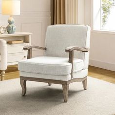 a white chair sitting on top of a wooden floor next to a lamp and dresser