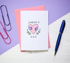 a card with the words sending a hug on it next to a pen and paper clip