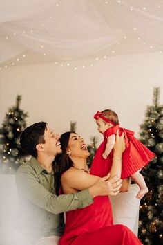 a man and woman holding a baby in front of a christmas tree