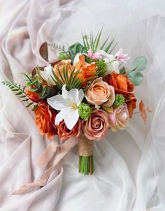 a bridal bouquet with orange, pink and white flowers on top of a bed