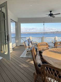 a large wooden deck with wicker chairs and table on it next to the ocean