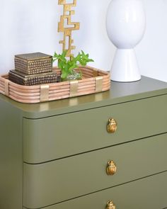 a green dresser with some plants on top of it and a white lamp in the background