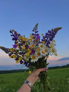 a hand holding a bouquet of wildflowers and daisies in a grassy field