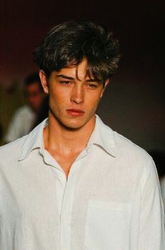 a young man in a white shirt is looking at the camera while he walks down the runway