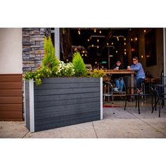 two men sitting at tables in front of a building with plants growing out of it