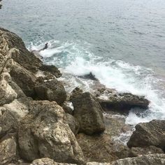 a man standing on top of a rocky cliff next to the ocean