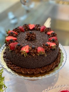 a chocolate cake with strawberries and blueberries on top sitting on a glass platter