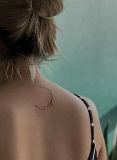 the back of a woman's neck with a small crescent tattoo on her left shoulder