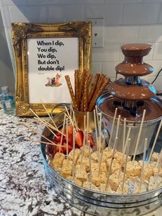 an assortment of snacks on sticks in a bowl next to a chocolate fountain and sign