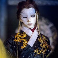 a close up of a doll wearing a black and gold outfit with chains on it's head