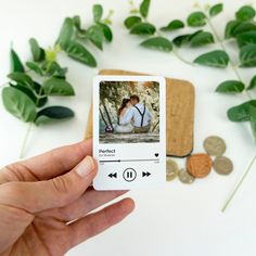 a person holding up an mp3 player to take a photo next to some leaves and coins