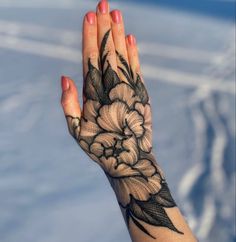 a woman's hand with a flower tattoo on her arm and the sky in the background