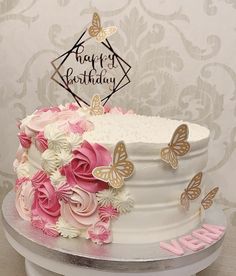 a white cake with pink flowers and butterflies on top is sitting on a table in front of a wall