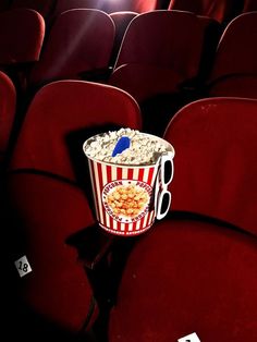 an empty bucket of popcorn sitting in the middle of a row of red velvet seats