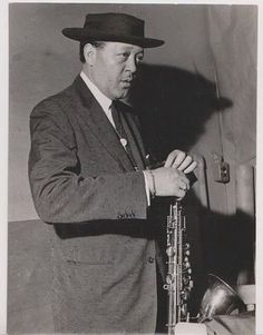 a man in a suit and hat holding a saxophone while standing next to a table