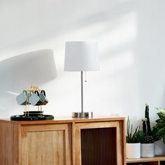 a lamp on top of a wooden cabinet next to a potted plant and other plants