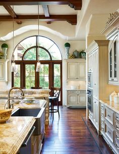 a large kitchen with white cabinets and wood flooring, along with an arched doorway leading to the dining room