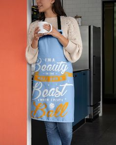 a woman is holding a coffee mug while standing next to a wall with an apron on it