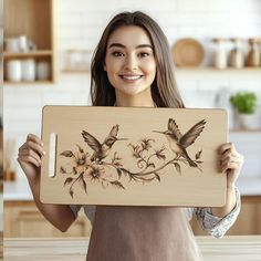 a woman holding up a wooden plaque with flowers and birds painted on it in the kitchen