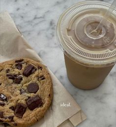 a cookie next to a cup of coffee on top of a marble table with paper napkins