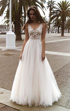 a woman in a white wedding dress is standing on the street with palm trees behind her