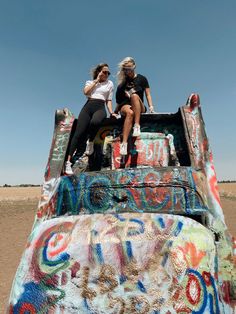 two women are sitting on the back of a truck covered in graffiti and spray paint