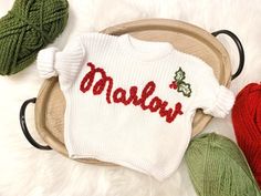 two knitted christmas sweaters sitting on top of a wooden tray next to balls of yarn