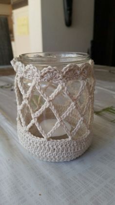 a crocheted candle holder sitting on top of a white cloth covered tablecloth