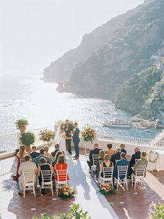 a wedding ceremony on the terrace overlooking the ocean and boats in the water, with people sitting at tables